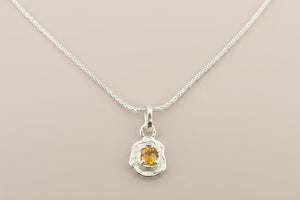 Silver pendant with a yellow gemstone on a gray background