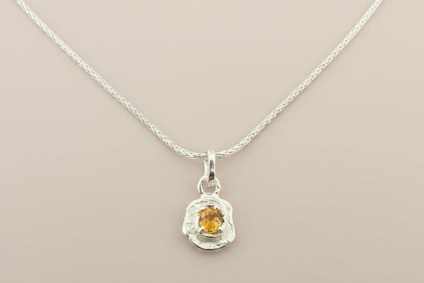 Silver pendant with a yellow gemstone on a gray background