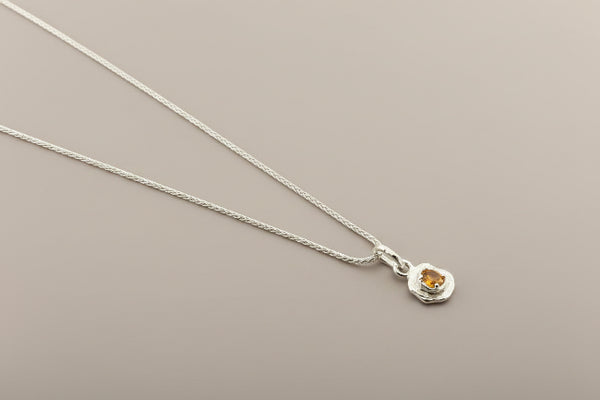 Silver necklace with a pendant featuring a yellow gemstone on a gray background