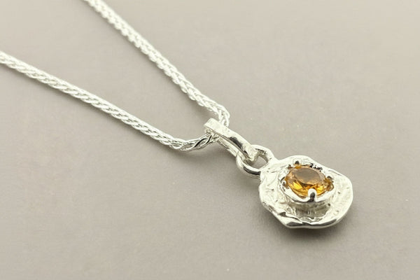 Silver necklace with a pendant featuring a yellow gemstone on a gray background