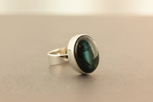Silver ring with a green cat's-eye gemstone on a gray background