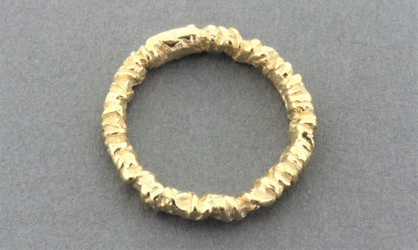A textured gold band ring with a heavily hammered, organic, and ridged surface, shown on a neutral gray background.