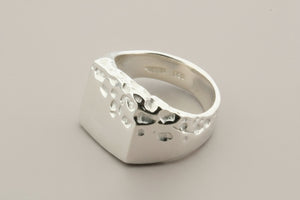 Silver ring with textured design on a gray background