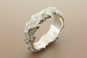 Silver ring with textured design on a dark gray background