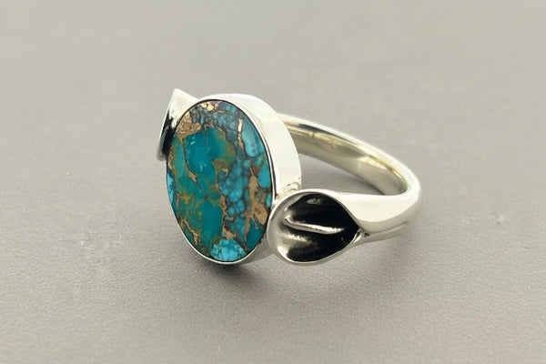 A sterling silver ring featuring a large circle turquoise stone with brown matrix veining, set against a dark gray textured background.