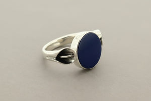 A sterling silver ring featuring a large, smooth oval dark blue lapis lazuli stone, photographed on a textured dark gray background.