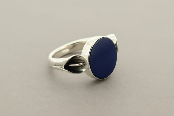 A sterling silver ring featuring a large, smooth oval dark blue lapis lazuli stone, photographed on a textured dark gray background.