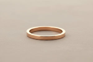 A minimalist, polished rose gold band ring resting on a dark gray textured surface.