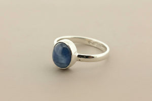 A sterling silver ring featuring a smooth, oval-shaped dark blue cabochon gemstone, displayed on a textured dark gray surface.