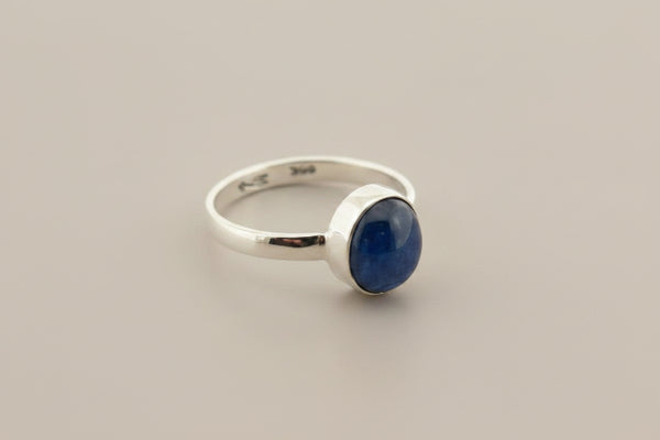 A sterling silver ring featuring a round, bezel-set dark blue gemstone, photographed on a dark gray textured surface.
