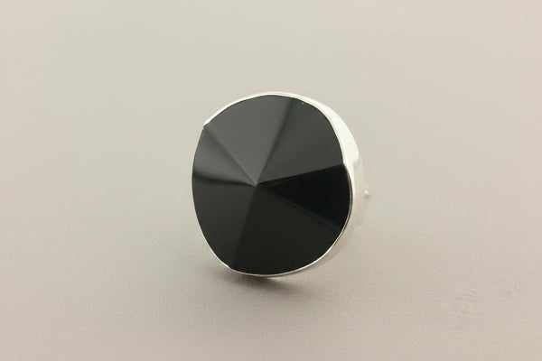 A silver-toned ring featuring a large, faceted black onyx cabochon, photographed on a dark gray textured surface.