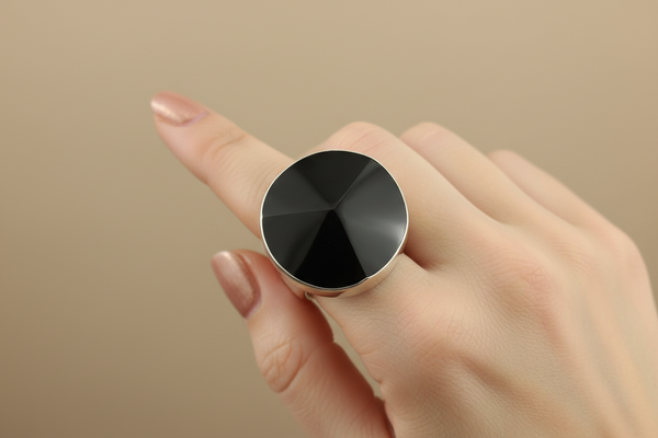 A silver-toned ring featuring a large, faceted black onyx cabochon, photographed on a dark gray textured surface.