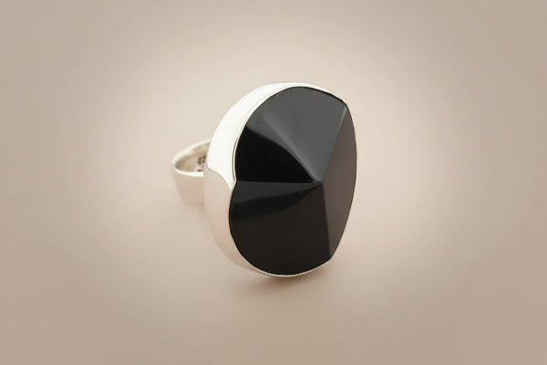 A silver ring featuring a large, faceted black onyx stone, photographed on a dark gray textured surface.