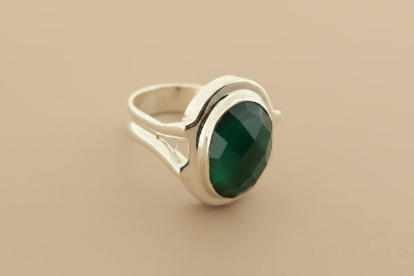 A silver ring featuring a large, oval-cut dark green faceted gemstone, photographed on a textured dark gray surface.