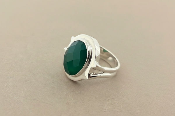 A sterling silver ring featuring a large, oval-cut dark green stone, photographed on a dark gray textured surface.