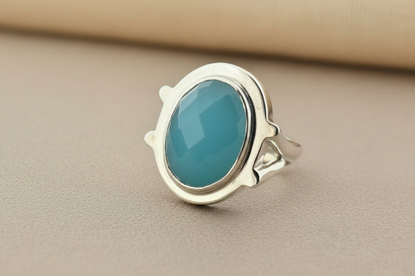 A sterling silver ring featuring an oval-cut turquoise stone, displayed on a dark gray textured surface.