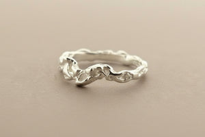 A textured sterling silver ring with a wavy, organic pattern, displayed on a dark gray background.