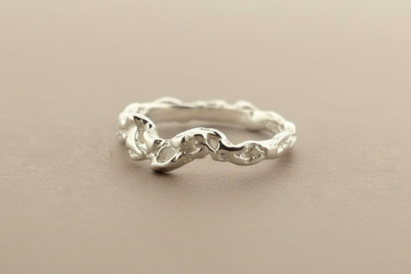A textured sterling silver ring with a wavy, organic pattern, displayed on a dark gray background.