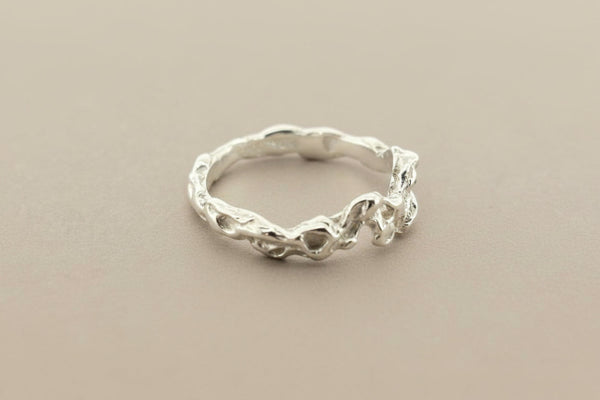A textured sterling silver ring with an organic, wavy, tree-bark-like band, photographed on a dark gray background.