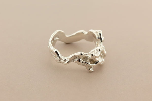 A silver ring with an organic, textured, tree-bark-like shape, photographed on a dark gray background.