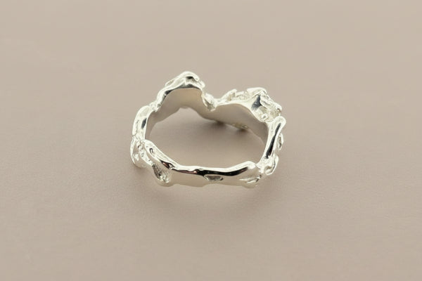 A silver ring with an organic, bark-like textured design, photographed on a dark gray background.