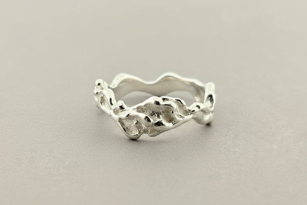 A silver ring with an organic, wavy, textured band, photographed on a dark gray textured surface.