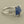 Load image into Gallery viewer, A sterling silver ring featuring a rough, faceted blue stone set in a four-prong setting, displayed on a dark gray textured surface.
