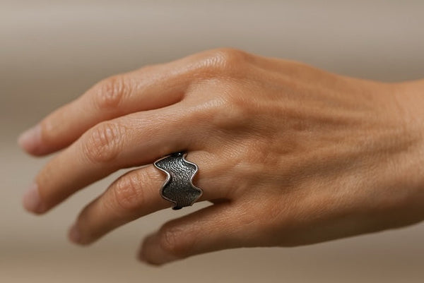 Hand wearing a silver ring on a beige background