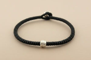 Black braided bracelet with silver beads on a gray background