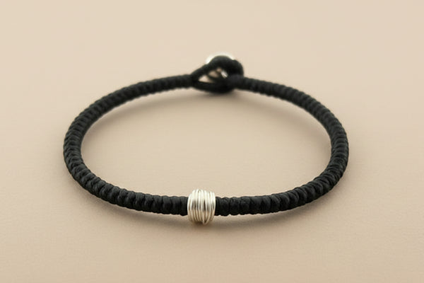 Black braided bracelet with silver beads on a gray background