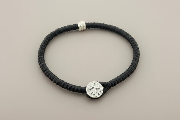 Black bracelet with a textured silver charm on a gray background