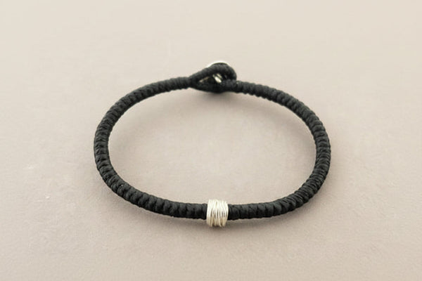 Black braided bracelet with a silver clasp on a gray background