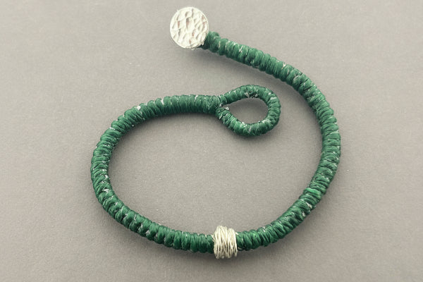 Green beaded bracelet with silver accents on a gray background