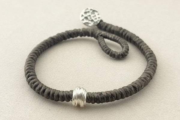 Bracelet with textured brown cord and silver metal ends on a gray background
