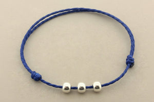 Blue cord bracelet with three silver beads on a gray background