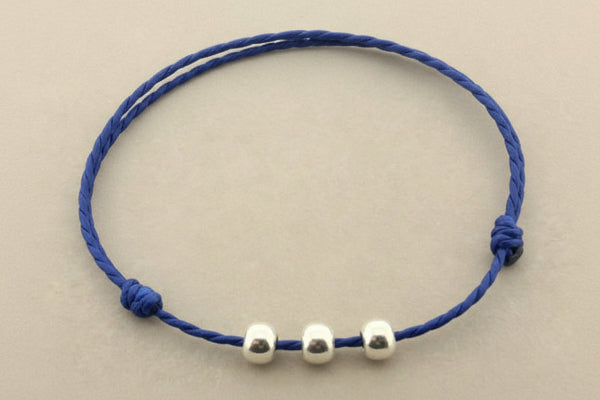 Blue cord bracelet with three silver beads on a gray background