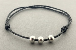 Black cord bracelet with three silver beads on a gray background
