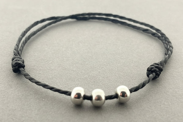 Black cord bracelet with three silver beads on a gray background