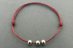 Red string bracelet with three silver beads on a gray background