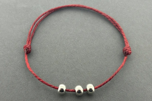 Red string bracelet with three silver beads on a gray background
