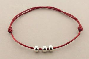 Red bracelet with three silver beads on a gray background