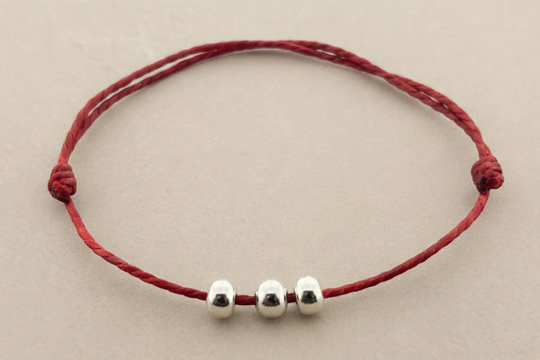 Red bracelet with three silver beads on a gray background