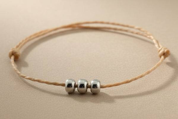 Beige cord bracelet with three silver beads on a gray background