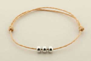 Bracelet with three silver beads on a beige cord against a gray background