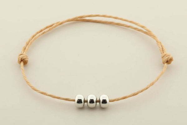 Bracelet with three silver beads on a beige cord against a gray background