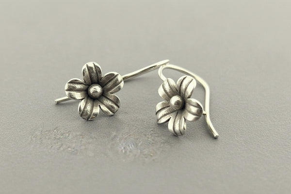 Pair of silver flower-shaped earrings on a gray background