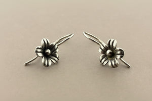 Pair of silver flower-shaped earrings on a gray background