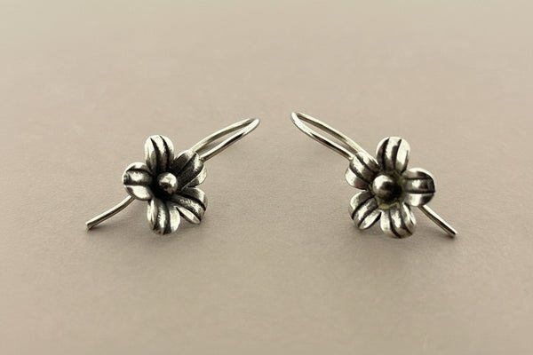 Pair of silver flower-shaped earrings on a gray background