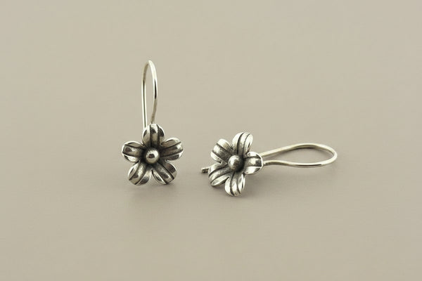 Pair of silver flower-shaped earrings on a gray background