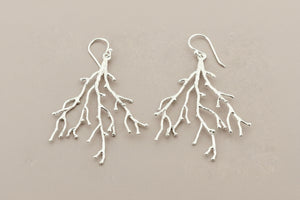 Silver branch-like earrings on a gray background